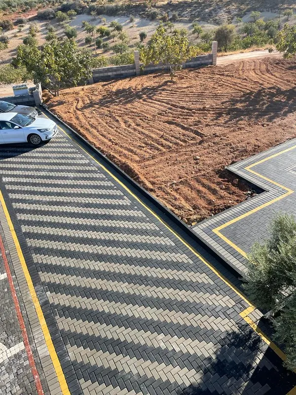 Yukarıdan görünen gri ve antrasit balık sırtı kilit parke zemin, sarı şeritli kenarlar ve yanında tesviye edilmiş toprak alan